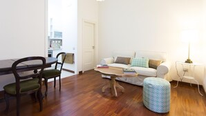 Ein modernes Wohnzimmer mit Esstisch, Stühlen, einer Couch und einem gemusterten Hocker.