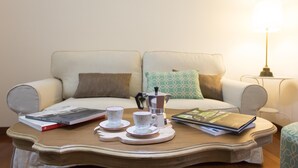 Ein gemütliches Wohnzimmer mit einer Couch, einem Couchtisch, einer Lampe sowie einigen Büchern und Tassen.