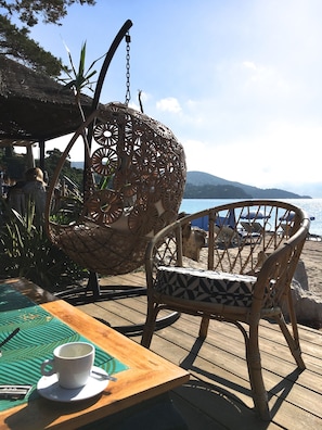 A wooden deck with a wicker chair and a hanging chair overlooking a beach. - Apartment in edge of sea. Residence of standing (Le Lavandou)