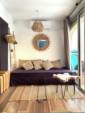 A modern bedroom with a large bed, a hanging rattan light fixture, a mirror with a bamboo frame, and a view of the outside. - Apartment in edge of sea. Residence of standing (Le Lavandou)