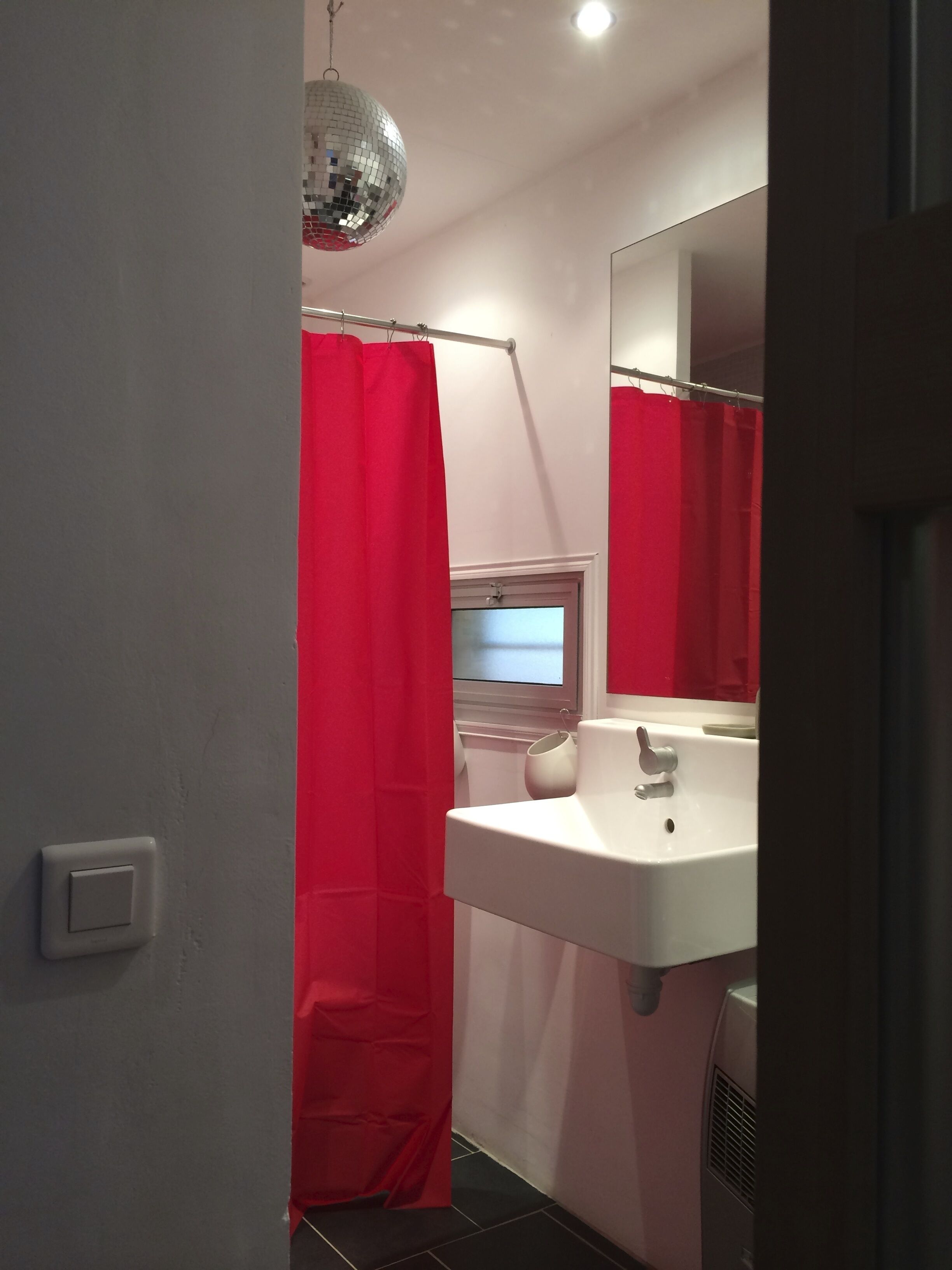 Ein Badezimmer mit weißem Waschbecken, rotem Duschvorhang und einer Discokugel-Lampe.