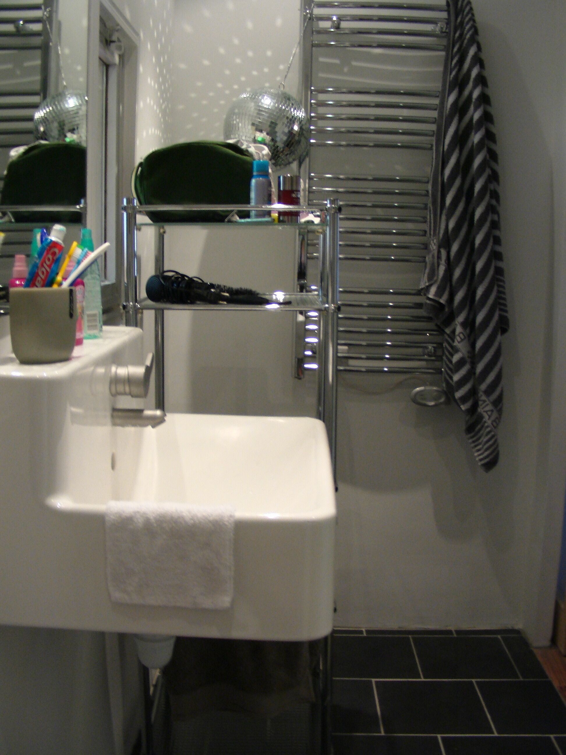 Une salle de bain avec un lavabo blanc, un miroir, une serviette, un porte-brosse à dents et une serviette à rayures accrochée au mur.