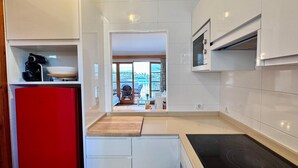 Et moderne køkken med hvide skabe, et rødt køleskab, en indbygget ovn og udsigt til en balkon med udendørs siddepladser.