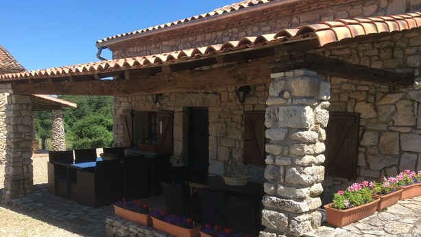 A stone building with a tiled roof, outdoor seating, and flower planters.
