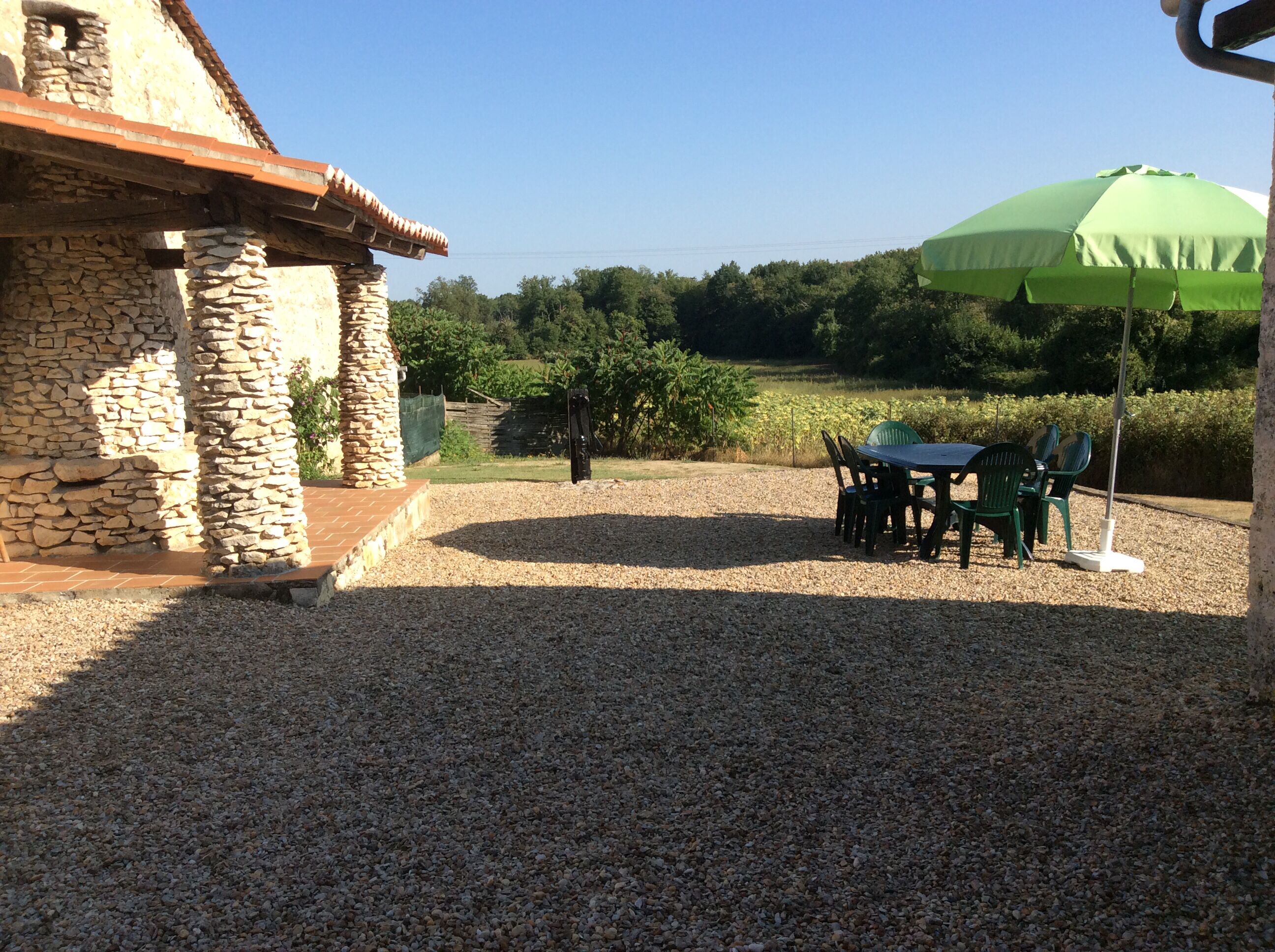 A patio with a stone wall, a table with chairs, and a green umbrella.
