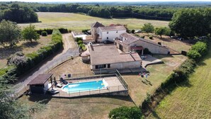 A large house with a swimming pool, surrounded by a fenced yard and a dirt road.