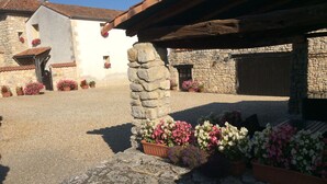 A stone building with a rustic roof, potted flowers, and a gravel courtyard.