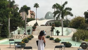 A poolside area with chairs and a fountain, surrounded by palm trees and a building with a dome structure. - Spacious town house WiFi, Air con, central location sought after Belgravia Club (Estepona)