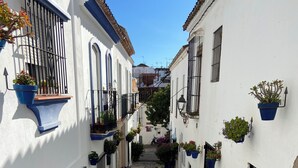 A narrow cobblestone street flanked by white buildings with black railings and potted plants. - Spacious town house WiFi, Air con, central location sought after Belgravia Club (Estepona)