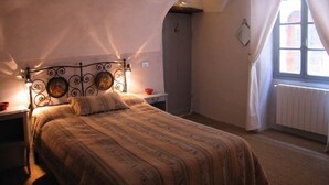 A bedroom with a bed, a nightstand, a wall-mounted picture, a window with curtains, and a radiator. - traditional house in  beautiful APRICALE, Liguria, experience the real Italy! (Apricale)