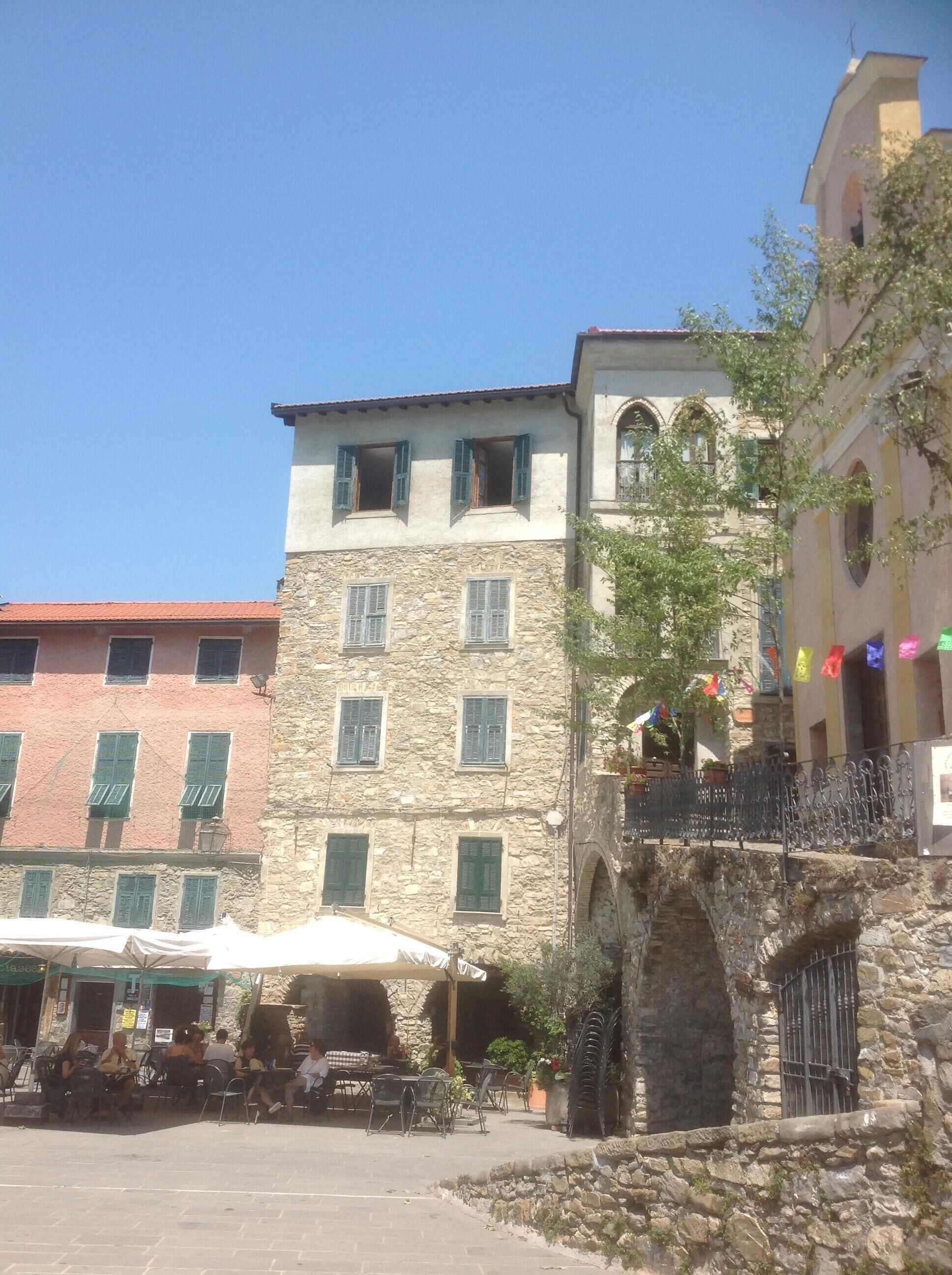A stone building with multiple windows and a balcony. There is a small outdoor seating area with tables and chairs.