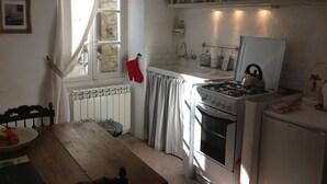 A kitchen with a gas stove, oven, and a sink. There is a window with curtains, a radiator, and a shelf above the sink. - traditional house in  beautiful APRICALE, Liguria, experience the real Italy! (Apricale)