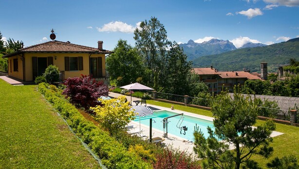 A residential area with a swimming pool, lush greenery, and a mountain backdrop. - Spacious 5 bedroom villa with private pool, full wheelchair access with lift (Garfagnaana)