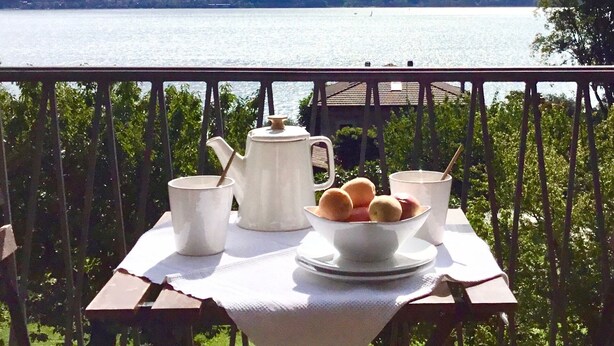 Une table dressée sur un balcon, avec vue sur un lac et des montagnes.