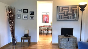 Un salon avec un plancher en bois, une télévision, une lampe et, au fond, un coin repas.