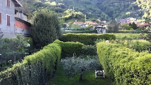 Un paysage montagneux agrémenté d’un jardin bien entretenu, d’un bâtiment aux volets rouges et d’un village situé au loin.