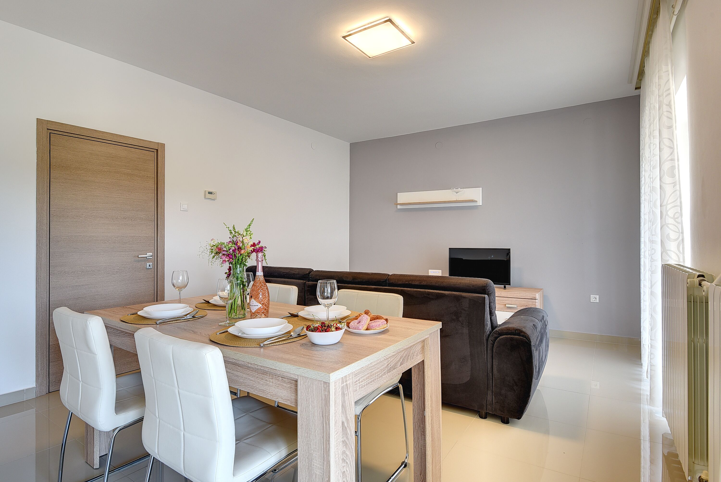 A modern dining area with a wooden table, white chairs, and a brown sofa.