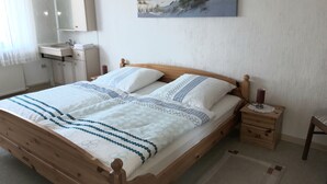 A bedroom with a wooden bed, a bedside table, a nightstand, a mirror, a painting, and a bathroom with a sink and toilet. - Quiet Non smoking apartment (approx 80sqm.) Located right on the edge. (Holzerath)