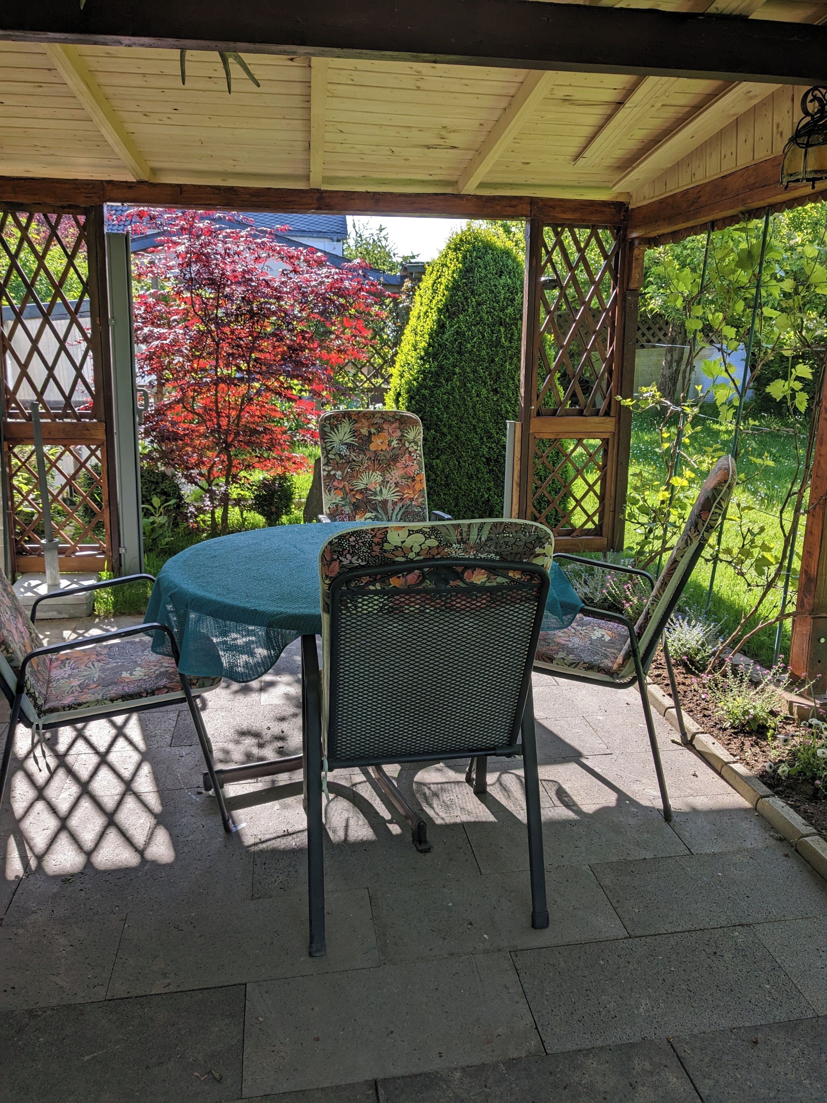 Une terrasse couverte avec une table et des chaises, un plafond en bois et une vue sur le jardin.