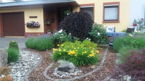 A residential garden with a variety of plants, a stone pathway, and a house with a brown door and windows. - Quiet Non smoking apartment (approx 80sqm.) Located right on the edge. (Holzerath)