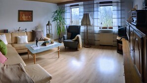 A living room with a sofa, armchair, and coffee table. There is a television, a lamp, and a plant. - Quiet Non smoking apartment (approx 80sqm.) Located right on the edge. (Holzerath)