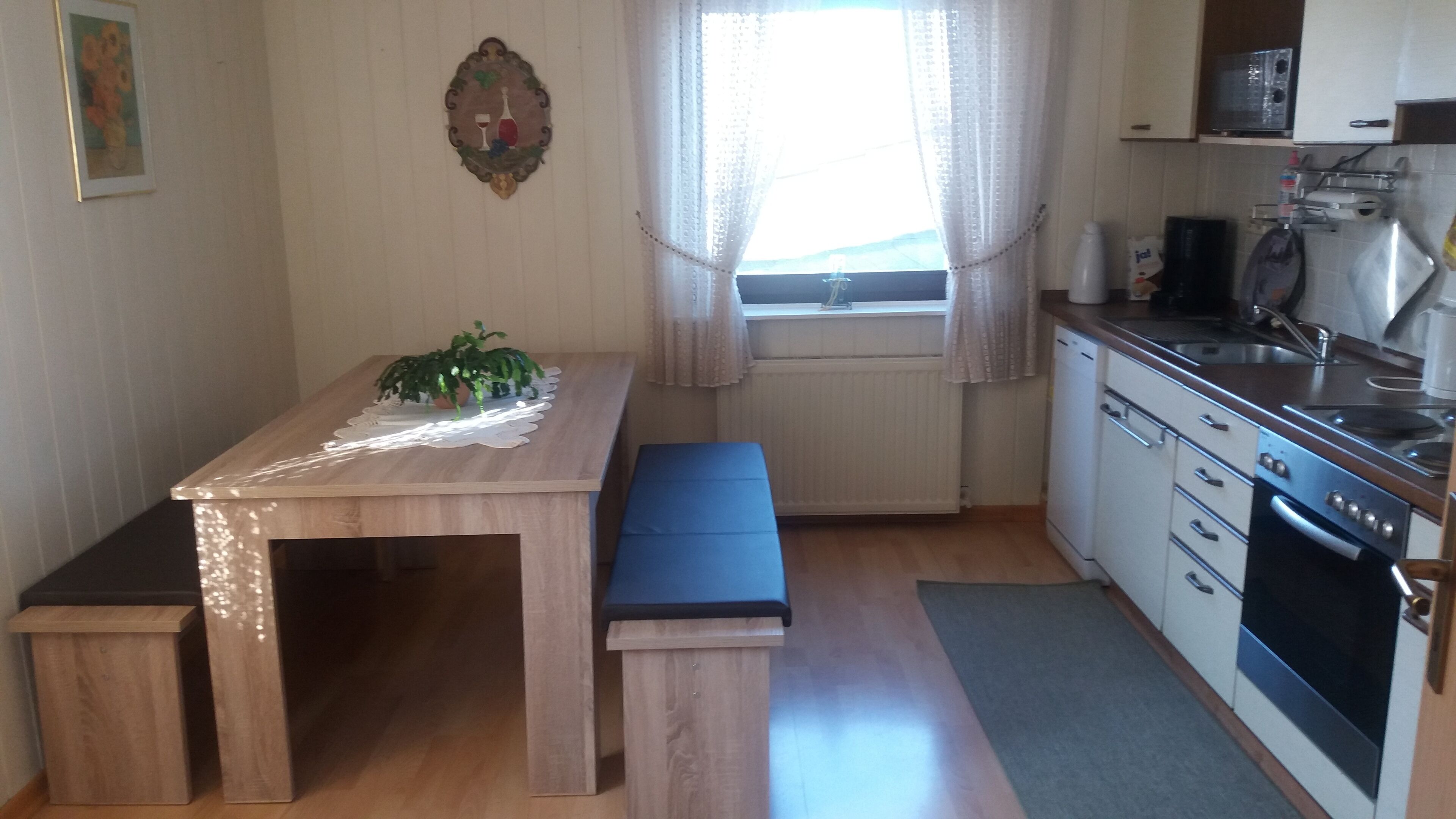 Une cuisine de taille réduite avec une table et un banc en bois, ainsi qu’une plante en pot.