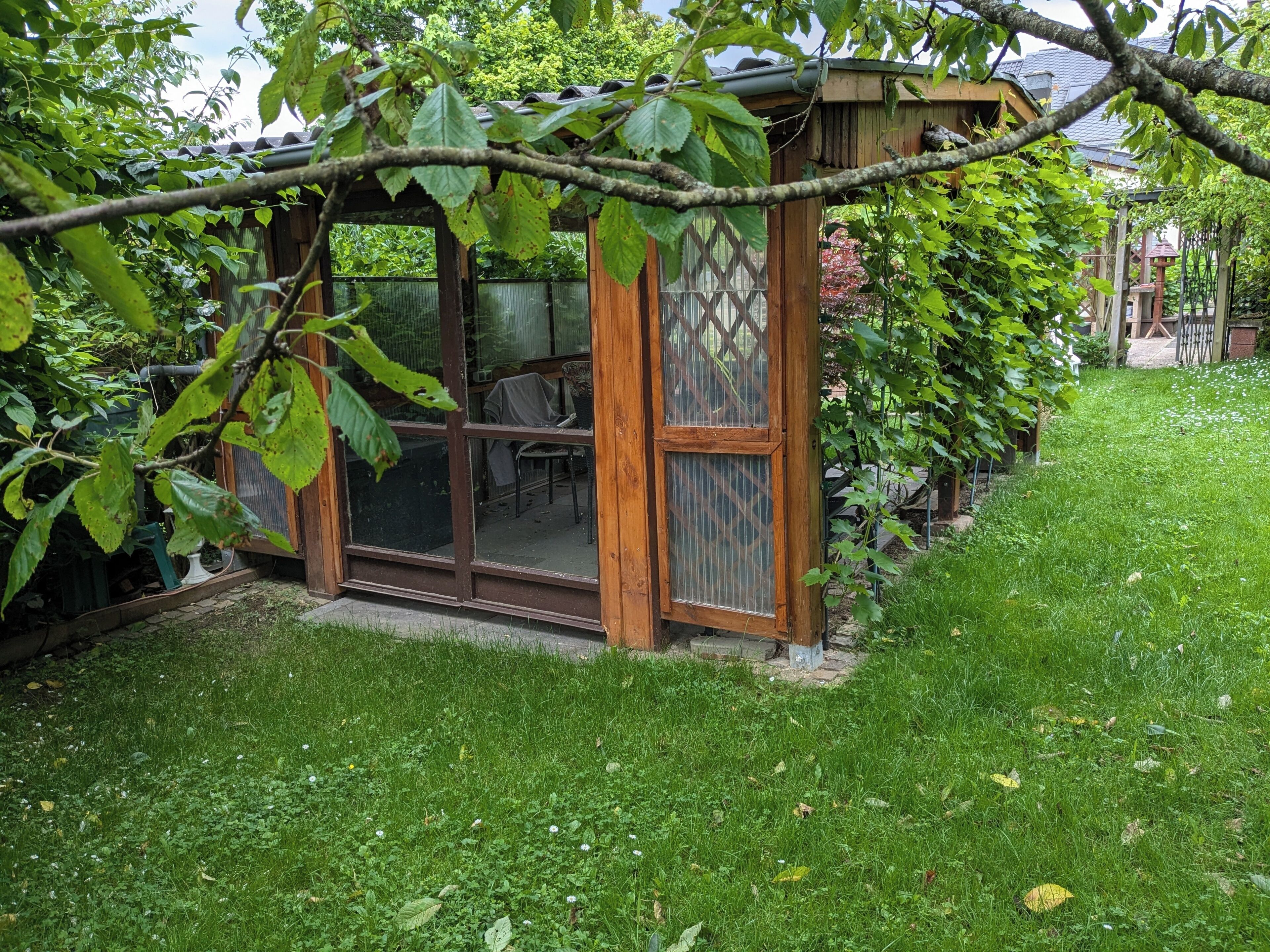 A wooden structure with a glass door and windows, surrounded by a grassy yard.