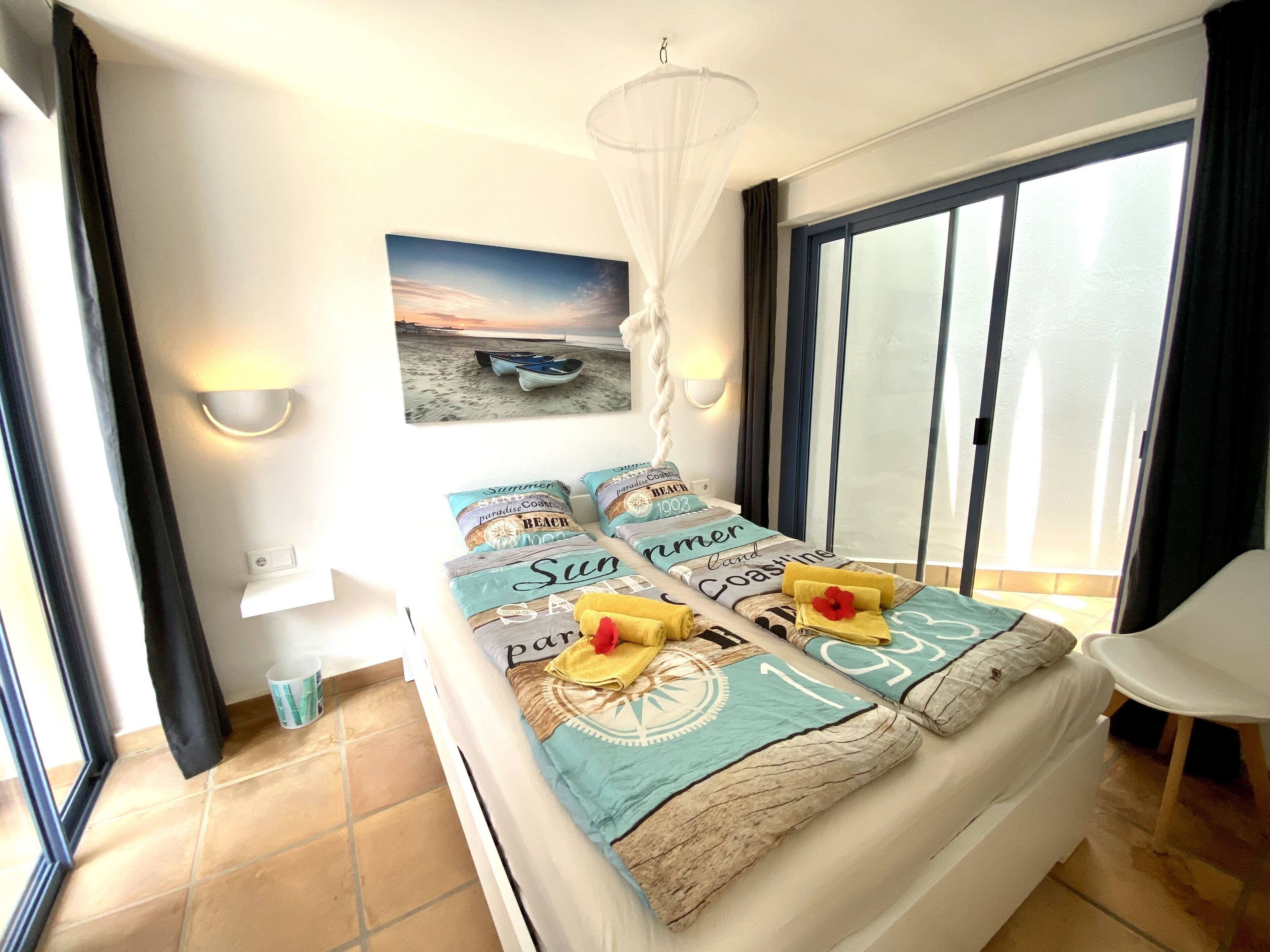 A bedroom with a bed, a view of the beach, and a chair.
