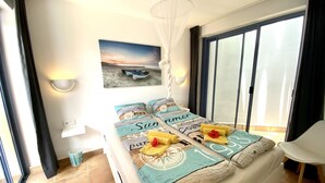 A bedroom with a bed, a beach-themed wall art, a window with curtains, and a bedside lamp. - Pool, few min from the sea, protected inner courtyard (Fuerteventura)