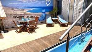 A poolside area with a view of a beach, a table with chairs, and lounge chairs. - Pool, few min from the sea, protected inner courtyard (Fuerteventura)