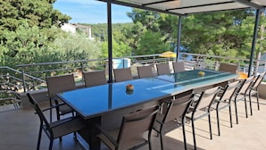 An outdoor patio with a glass-top table and chairs, surrounded by a metal railing, overlooking a lush green landscape.