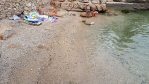 A rocky beach with a stone wall, clear water, and a beach umbrella.