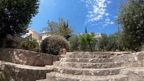 A set of stone steps leading up to a building with a white facade and red roof, surrounded by trees and shrubs.