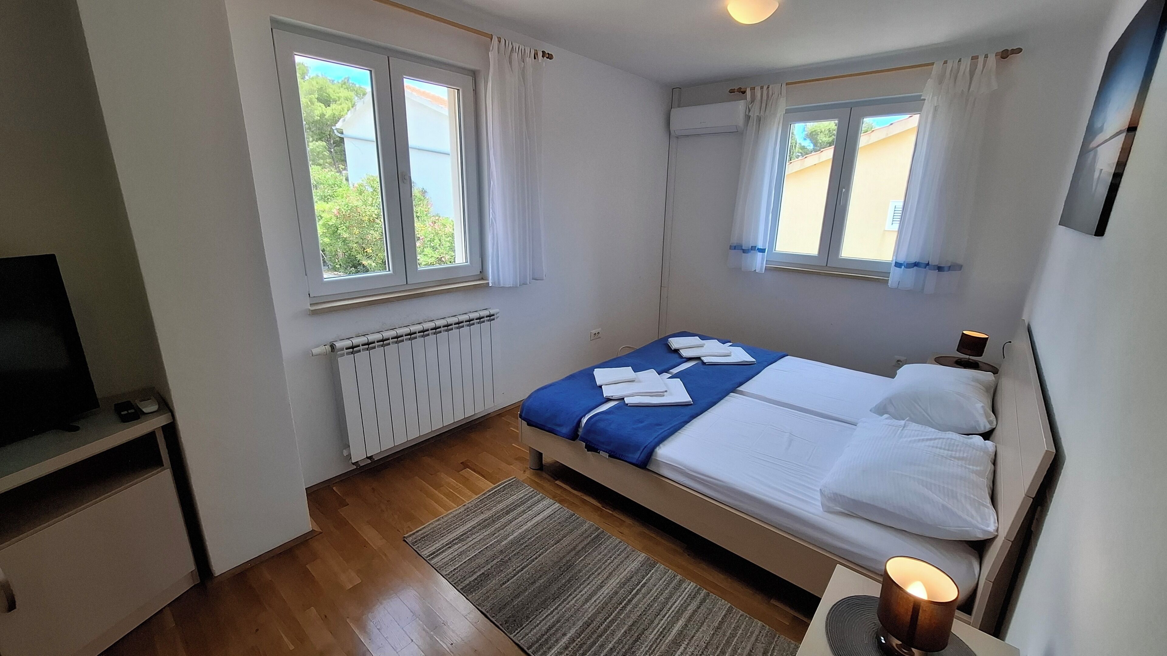 Un dormitorio con cama, televisor, radiador y ventanas.