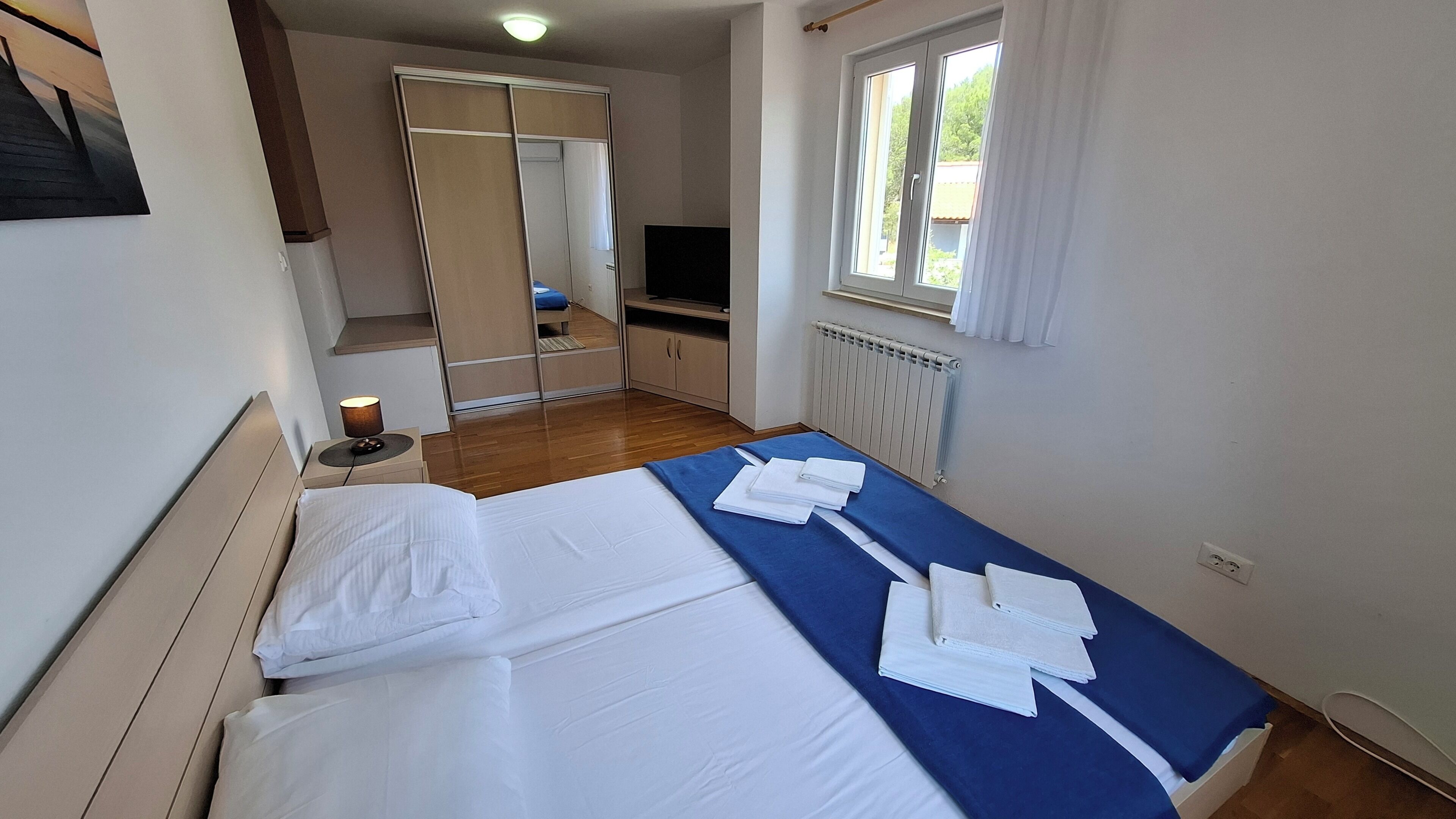 Ein Hotelzimmer mit zwei Betten, einem Kleiderschrank, einem Fernseher und einem Fenster mit Vorhängen.