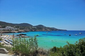 A coastal beach with clear turquoise waters, boats, and a rocky shoreline.