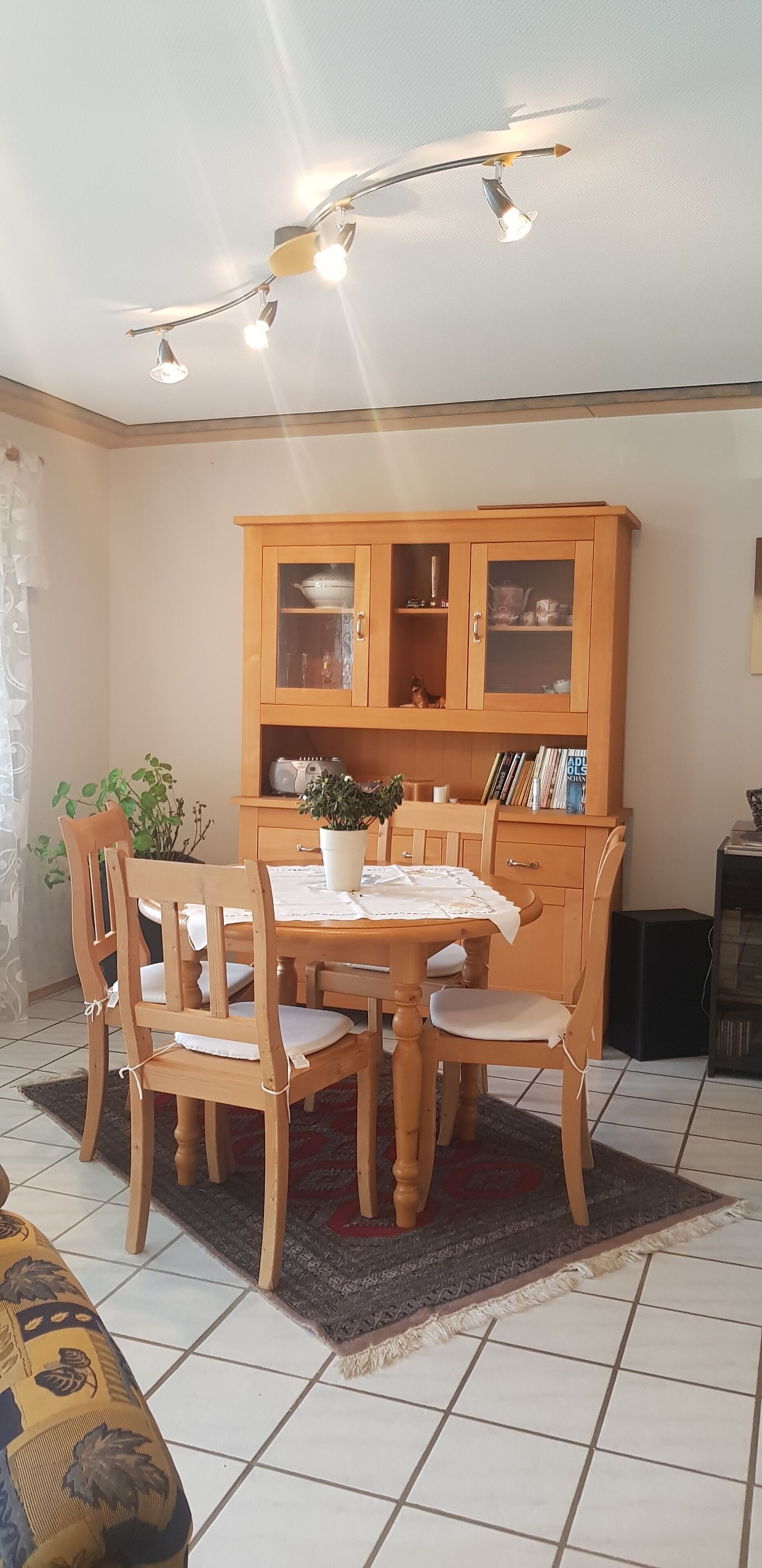 A dining area with a wooden table and chairs, a cabinet with glass doors, and a ceiling light fixture.