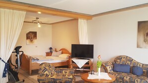 A hotel room with a bed, a TV, a sofa, a chair, a table, and a ceiling fan. - Comfortable apartment with pool for 2-6 people (110 sqm) (Ranschbach)