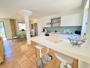 A modern kitchen with white cabinets, a central island with stools, and a dining area with chairs. - Villa with private pool, fiber optic internet, close to the sea, sheltered courtyard (Costa Calma)