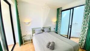 A neatly made bed with a rolled towel, a bedside table with a lamp, and a view of the sea through a sliding glass door. - Casa Barbara, private pool, internet, close to the ocean, sheltered courtyard/patio (Costa Calma)
