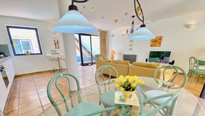 A modern living room with a glass dining table, teal chairs, a sofa, and a TV. - Casa Barbara, private pool, internet, close to the ocean, sheltered courtyard/patio (Costa Calma)