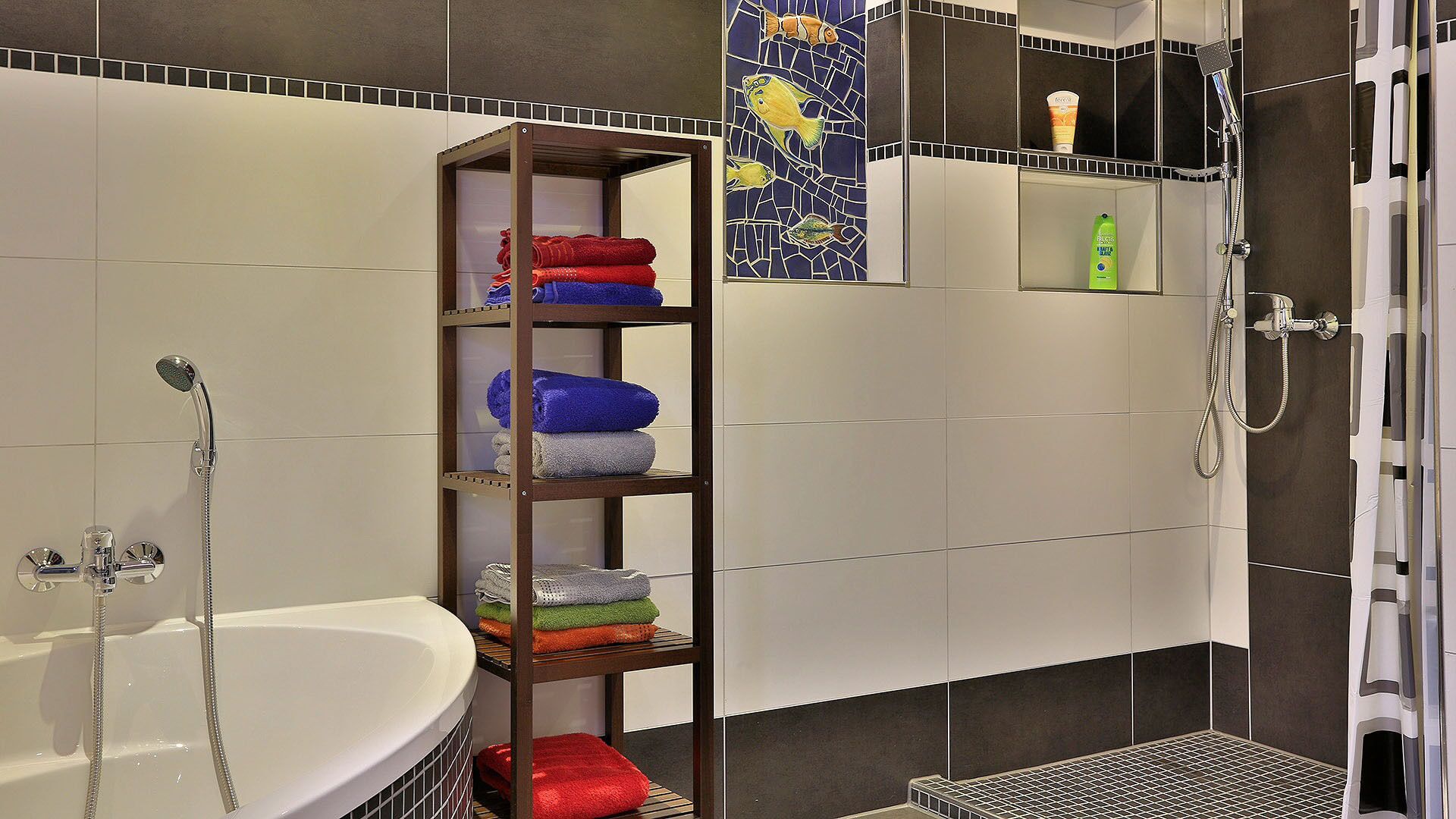 A modern bathroom with a white bathtub, a shower with a handheld showerhead, and a shelf with neatly folded towels in various colors.
