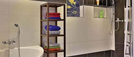 A modern bathroom with a white bathtub, a shower with a handheld showerhead, and a shelf with neatly folded towels in various colors.