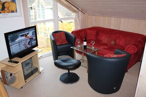 A living room with a red sofa, a black chair, a glass coffee table, and a television on a wooden stand.