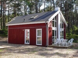 A small red cabin with a porch and white chairs, surrounded by trees.