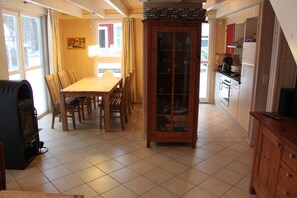 A dining area with a wooden table and chairs, a cabinet with glass doors, and a kitchen area with cabinets and appliances.