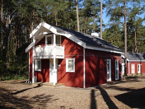 A red cabin with a balcony, surrounded by trees.