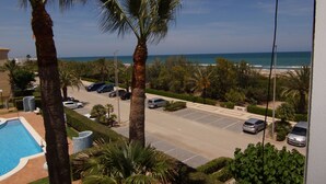 A view of a parking lot with several cars, a swimming pool, and palm trees.