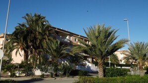 A multi-story building with balconies, surrounded by palm trees and a clear blue sky.