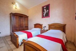 Een hotelkamer met twee houten bedden, een kledingkast, een nachtkastje en een wandlamp.